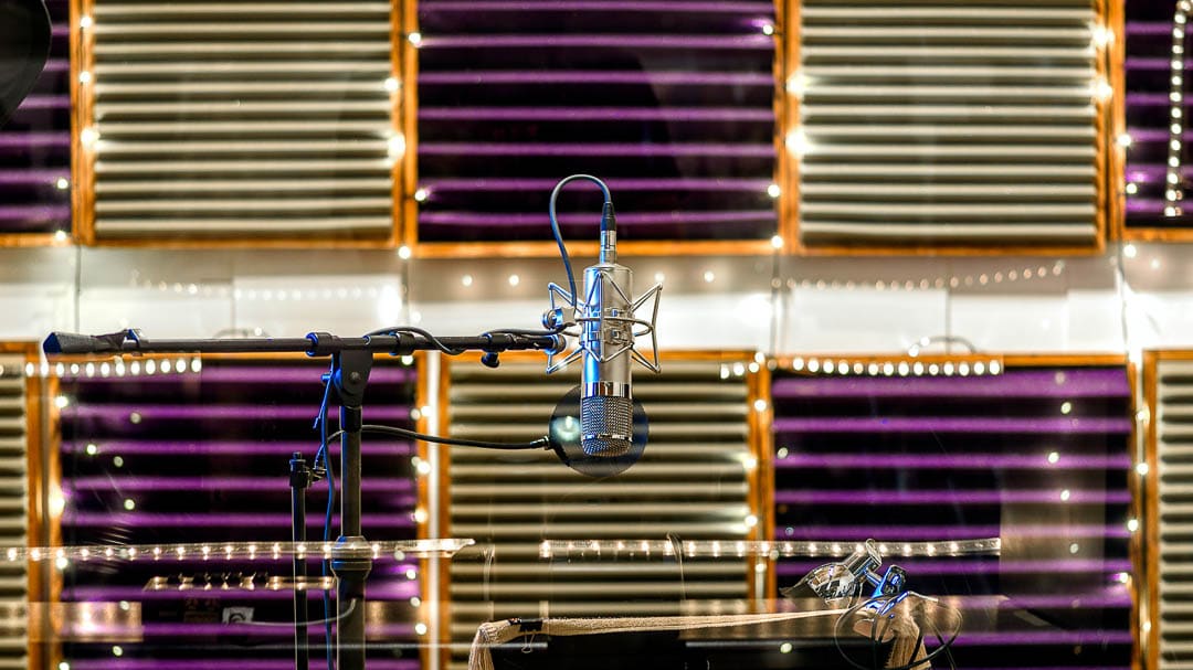 A tube microphone on a stand with pop filter in a recording studio with sound absorbers and fairy LED lights